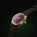 Carmine red Argos watch with a gold case and brown leather strap, a premium men’s timepiece.
