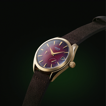 Carmine red Argos watch with a gold case and brown leather strap, a premium men’s timepiece.